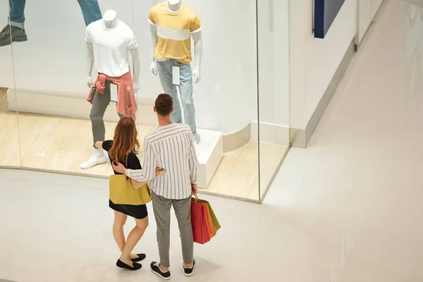 Hugging Young Couple Shopping Bags Looking Male Clothes Shop Window — Stock Photo, Image