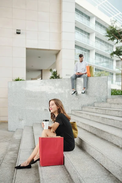 ショッピングモールの前で階段に座って販売にお金を費やしている若い白人女性 — ストック写真