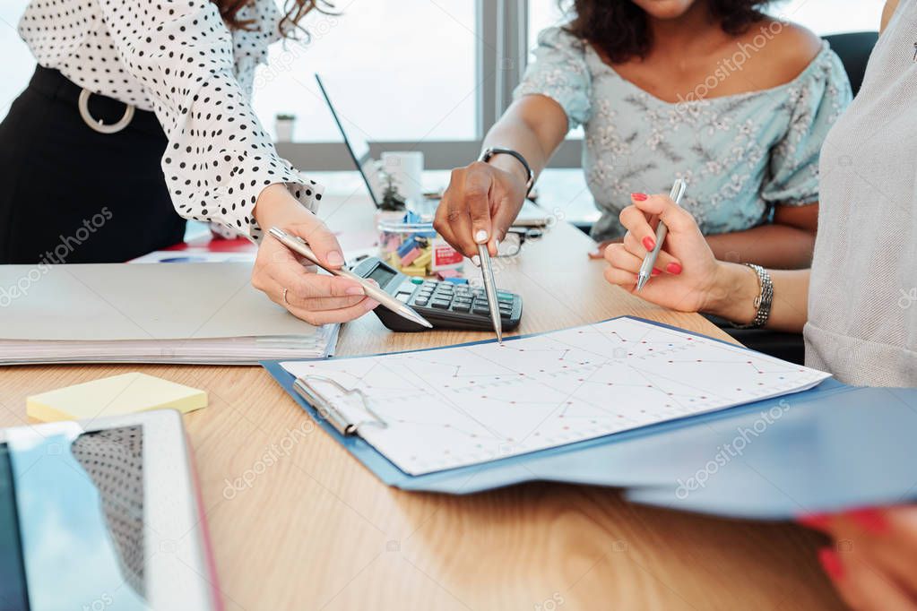 Hands of businesswomen pointing at document with financial chart and sales statistics