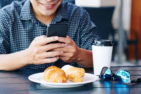 Usmívající Mladý Muž Kávou Croissant Snídani Čtení Textových Zpráv Smartphone — Stock fotografie