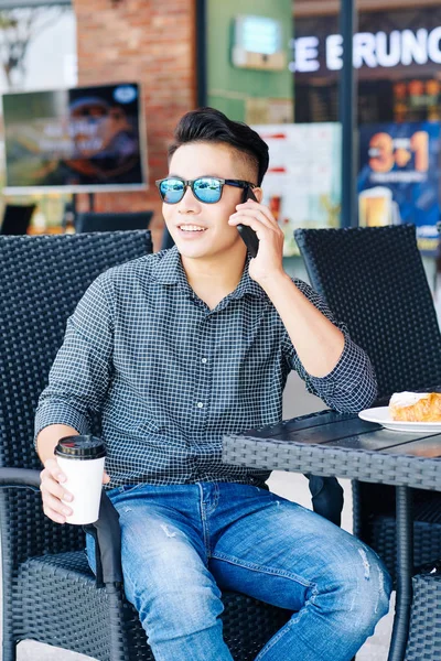 戴着太阳镜的快乐的年轻人坐在咖啡桌旁 吃着美味的早餐 打电话 — 图库照片