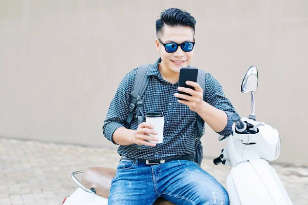 Glimlachende Jongeman Met Koffiebeker Scooter Meldingen Bekijken Zijn Smartphone — Stockfoto