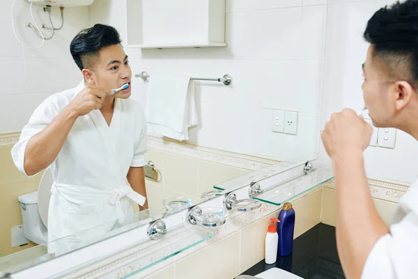 Przystojny Młody Azjata Białym Szlafroku Myje Zęby Przed Lustrem Rano — Zdjęcie stockowe