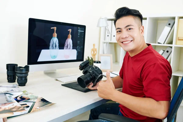 Portrét Šťastného Mladého Asijského Fotografa Sedícího Stolem Fotoaparátem Rukou Ukazujícího — Stock fotografie