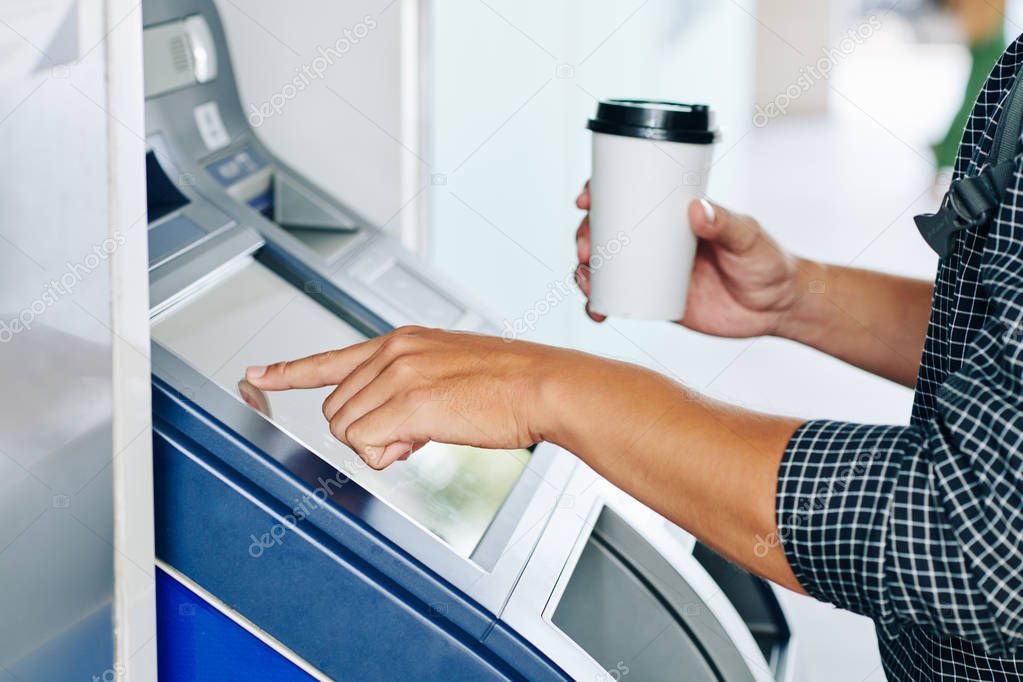 Hands of person with cup of coffee using bank terminal to transfer money 