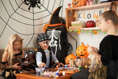 Kostüm giymiş bir grup arkadaş masada birlikte oturup Cadılar Bayramı partisi için renkli kağıtlardan el işleri yapıyorlar.