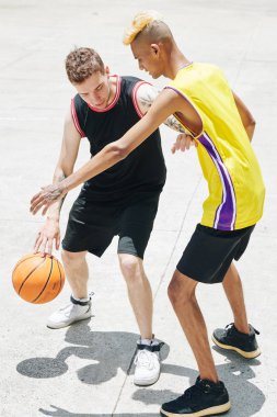Üniformalı çok ırklı gençler güneşli bir günde oyun alanında basketbol antrenmanı yapıyorlar.