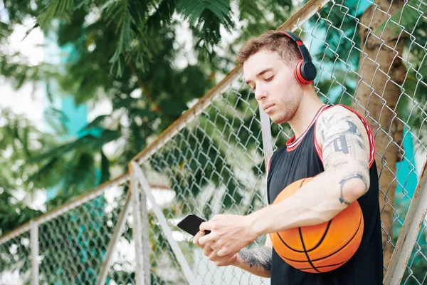 严重的年轻篮球运动员在耳机检查消息在他的智能手机 — 图库照片