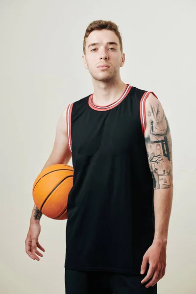 黒のユニフォーム保持ボールで自信深刻なバスケットボール選手とカメラを見て 白に分離 — ストック写真