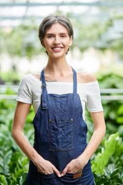Kot giymiş güzel bir kadın bahçenin bahçesinde duruyor ve kameraya gülümsüyor.