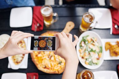 Adamın cep telefonunu elinde tutarken ve kafede otururken akşam yemeğinin fotoğrafını çekerken.