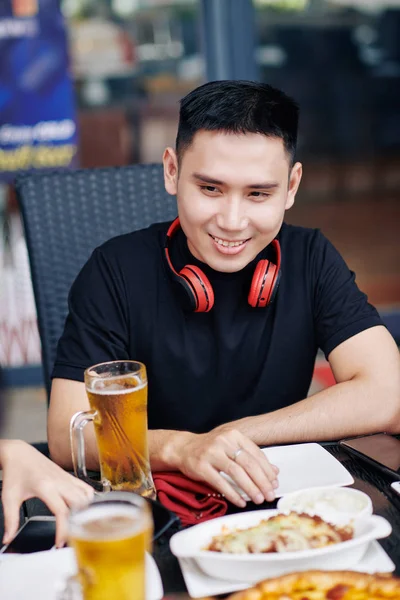 Boldog Ázsiai Fiatalember Asztalnál Étellel Alkoholos Italokkal Mosolyog Miközben Beszél — Stock Fotó
