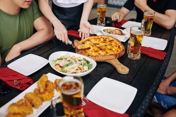 レストランで昼ご飯にピザやサラダやビールを食べながら木のテーブルに座る人は — ストック写真
