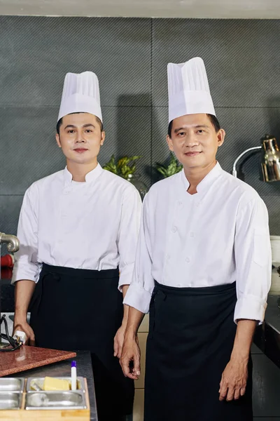 셔츠와 모자를 조수와 주방에서 카메라를 아시아 요리사의 — 스톡 사진