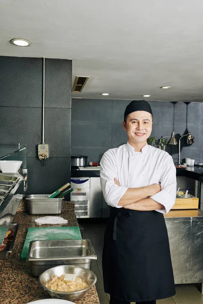 在餐馆厨房里 身穿制服的亚洲年轻厨师面带微笑地交叉着双臂站在镜头前的画像 — 图库照片