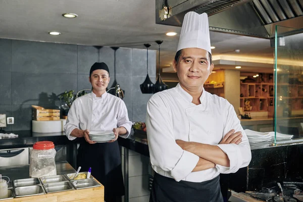 照片中 自信的亚洲厨师双手交叉地站在一起 看着镜头 年轻厨师在厨房的背景下准备食物 — 图库照片