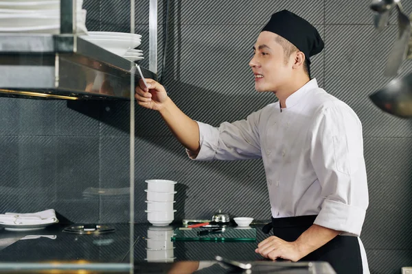 亚洲面带微笑的厨师看着粘贴便条 说他要下订单 准备在餐馆厨房里准备 — 图库照片