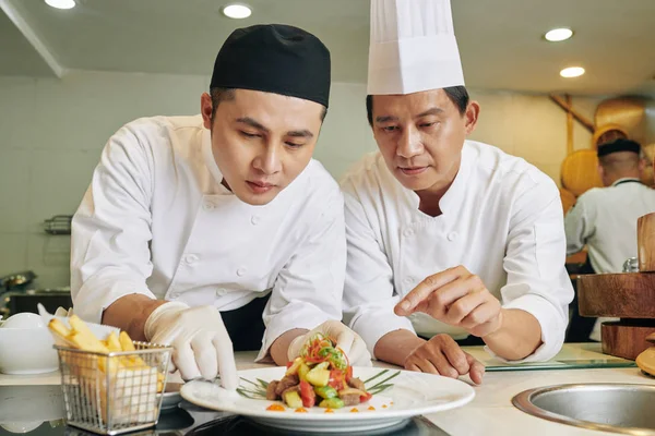亚洲成熟的厨师为他的学生开硕士班 教他在厨房里装饰菜 — 图库照片