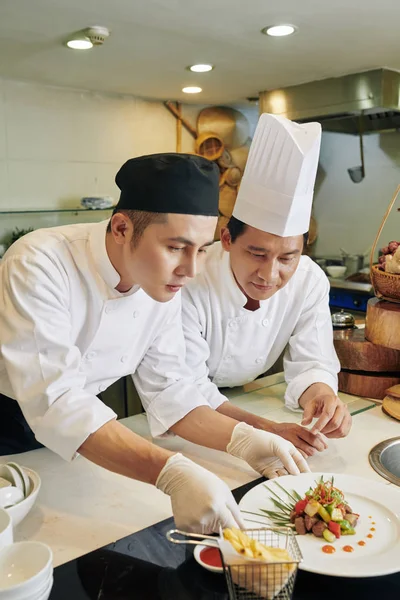 两个厨师一起工作 他们站在餐桌旁 在餐馆里装饰准备好的菜 — 图库照片