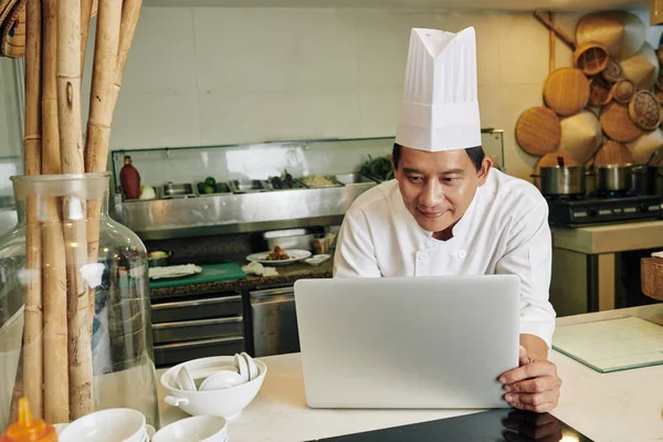 Azji Dojrzałe Szef Kuchni Mundurze Stojąc Kuchni Pracy Online Laptopie — Zdjęcie stockowe