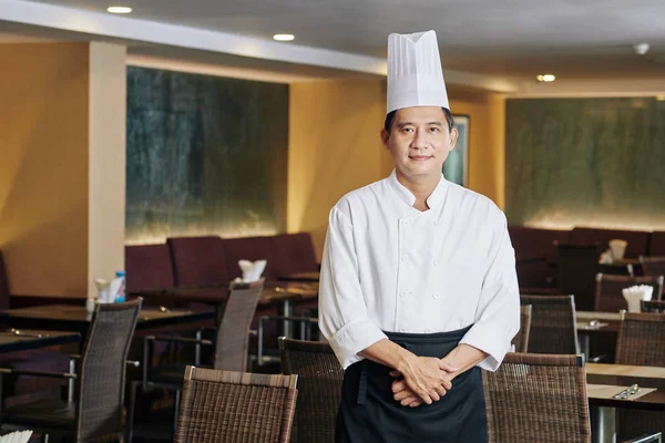 身着制服 头戴礼帽 站在餐厅空旷大厅看着相机的亚洲成熟厨师的画像 — 图库照片