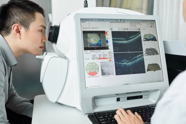 Asyalı genç bir hasta hastanede doktorla görüşünü özel tıbbi ekipmanlarla kontrol ediyor.