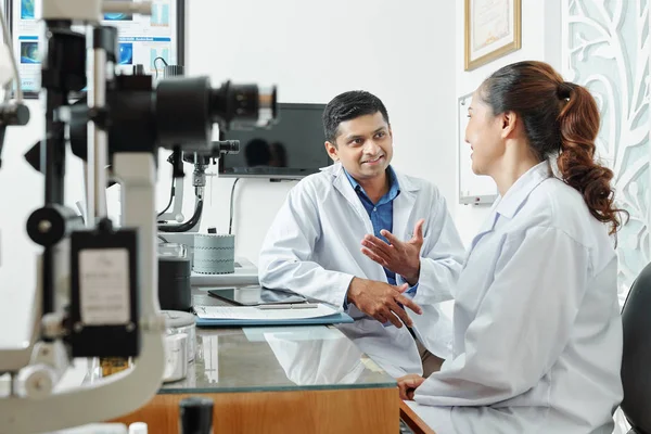 Indian Male Optometrist White Coat Sitting Discussing His Nurse Some — Stockfoto