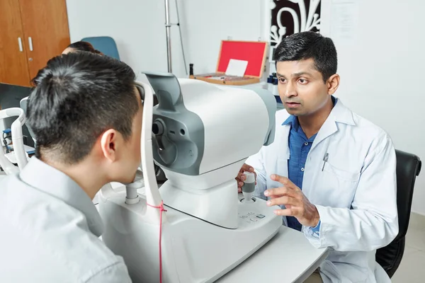 Indian serious doctor in white coat using medical equipment to examine his patient\'s eyesight at the hospital