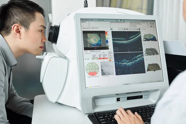 Asyalı genç bir hasta hastanede doktorla görüşünü özel tıbbi ekipmanlarla kontrol ediyor.