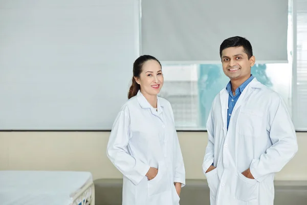 站在医院时穿着白衣的印度男医生和亚洲女医生对着相机微笑的画像 — 图库照片