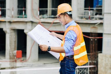 Gülümseyen Vietnamlı ustabaşı inşaat alanında çalışırken elindeki yeni binanın planlarını inceliyor.