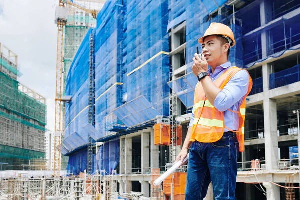 身穿明亮橙色背心的亚洲承包商使用对讲机与建筑工地的同事进行沟通 — 图库照片