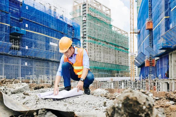 身穿橙色背心和硬礼帽的亚洲土木工程师在建筑工地室外工作时指着建筑图则 — 图库照片