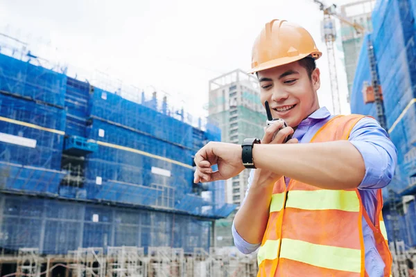 Smiling Vietnamese contractor talking to workers via walkie-talkie and making sure that everything will be done right on time
