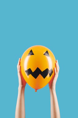 Cadılar Bayramı kutlaması için elinde korkunç yüzlü balon tutan kişi iki elini de mavi renkte soyutlamış.