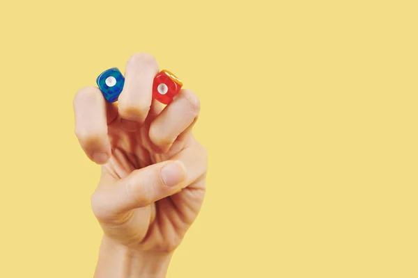黄色の背景に指の間に赤と青のサイコロを持つ人の手 — ストック写真