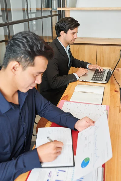 Empresário Asiático Sentado Mesa Examinando Gráficos Financeiros Fazendo Anotações Bloco — Fotografia de Stock