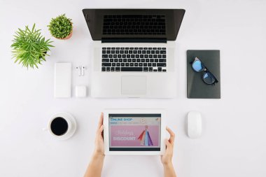 Ofis masasında oturan genç bir kadının elinde online dükkan uygulaması olan bir tablet bilgisayar.