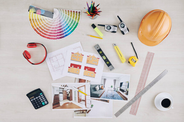 Table of professional architect with photos of interior visualization, house blueprint, hardhat and color palette