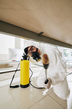 Koruyucu giysili temizlik işçisi evin her köşesine dezenfektan sıkıyor.