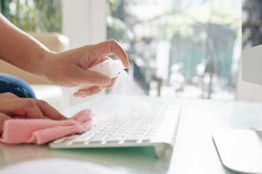Ofis masasına bakterileri öldürmek için dezenfektan sıkan kişinin elleri