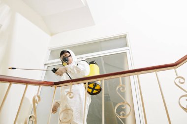 Tehlikeli hastalıkları yaymamak için beyaz koruyucu giysili temizlik işçisi hastanedeki merdivenleri dezenfekte ediyor.
