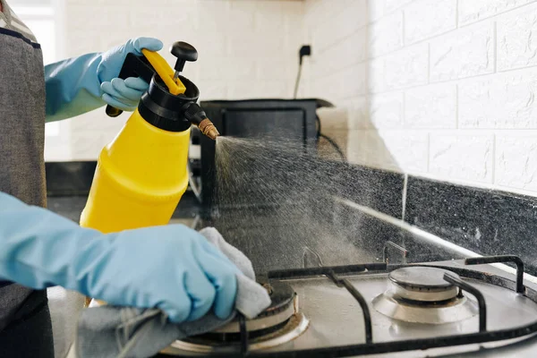 家庭主妇用洗涤剂喷洒厨房炉灶以消除油污的特写图像 — 图库照片
