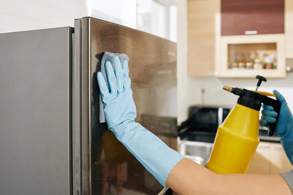ゴム手袋の女性のクローズアップイメージ布やスプレーボトルでステンレス製の冷蔵庫を掃除します — ストック写真