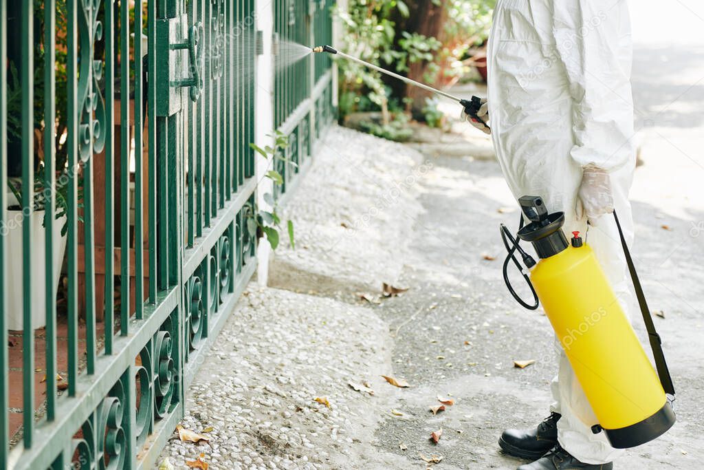 Cropped image of technician spraying fence with chemical to prevent spreading of pneumonia virus in city