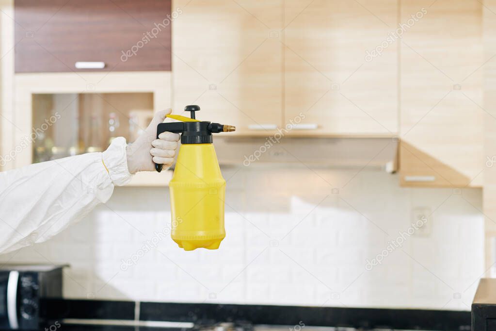 Gloved hand of technician holding bottle of detergent that help to get rid of viruses, bacteria and insects in house