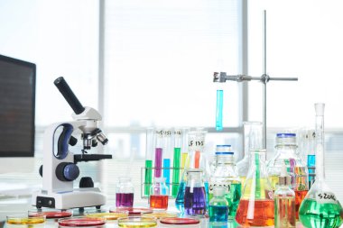 Mikroskop, mataralar, test tüpleri ve laboratuardaki masalarda renkli sıvılar bulunan petri kapları.