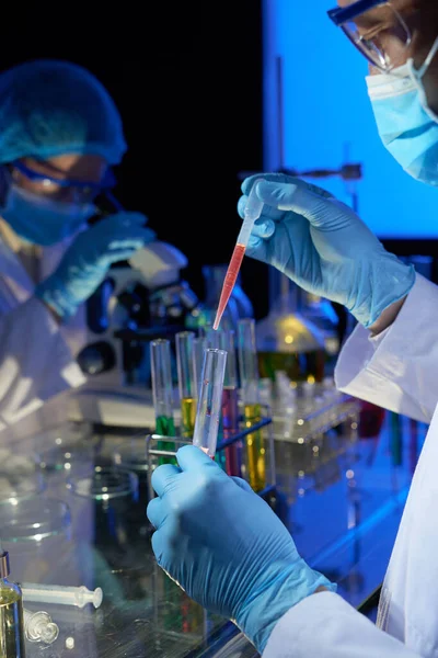 実験室の技術者はワクチンに取り組むときガラスのテスト管に赤い試薬のいくつかの滴を追加します — ストック写真