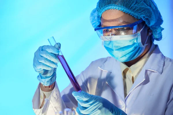 戴着医用口罩和防护眼镜的亚洲科学家正在研究用红色透明液体做试管的疫苗 — 图库照片