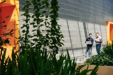 Ofis koridorunda dizüstü bilgisayarla yürüyen ve projeleri ve iş sonuçlarını tartışan pozitif iş adamları